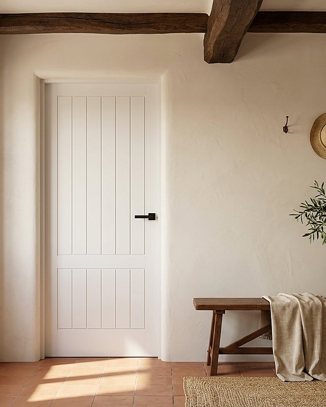 Puerta lacada blanca rústica de tablillas verticales en dos cuerpos, estancia encalada con vigas de madera. Imagen ilustrativa.